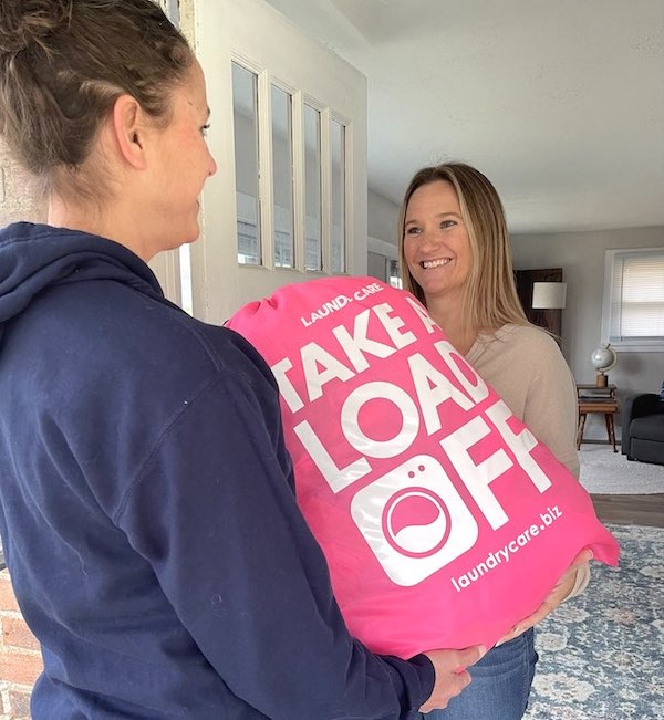 Happy Laundry Care client standing at front door with filled pink Laundry Care bag.